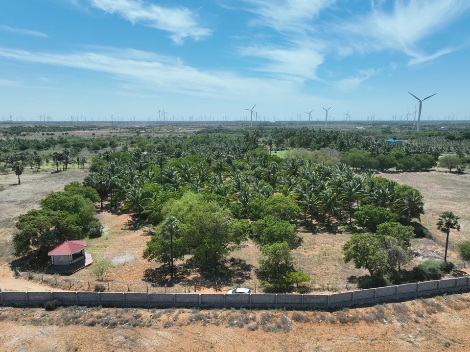 Wide aerial view of the plot and its surrounding open land under a clear sky